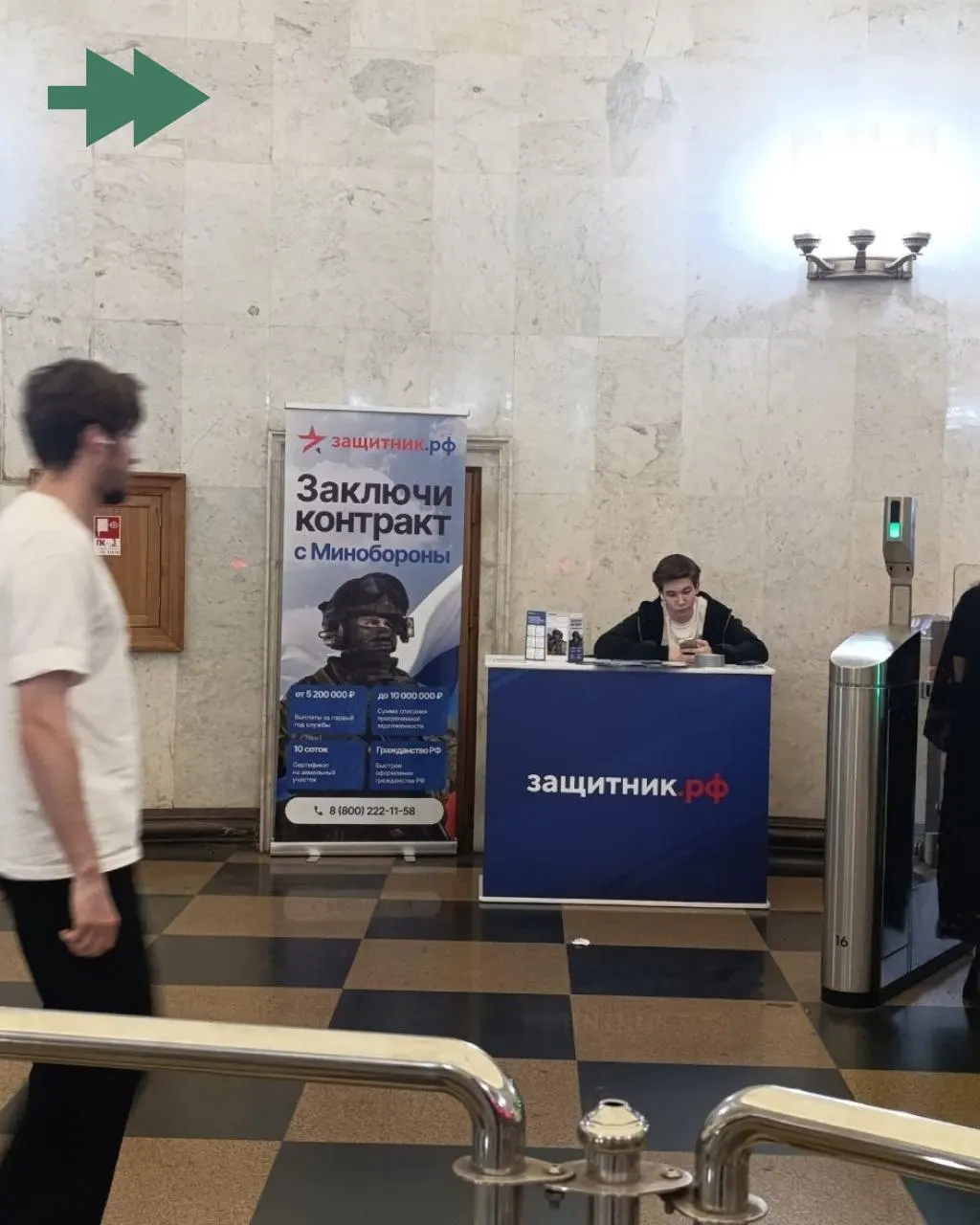 У турникетов станции Москвы обнаружена стойка с рекламой контракта на военную службу; рядом рекрутер предлагает подписать контракт.
